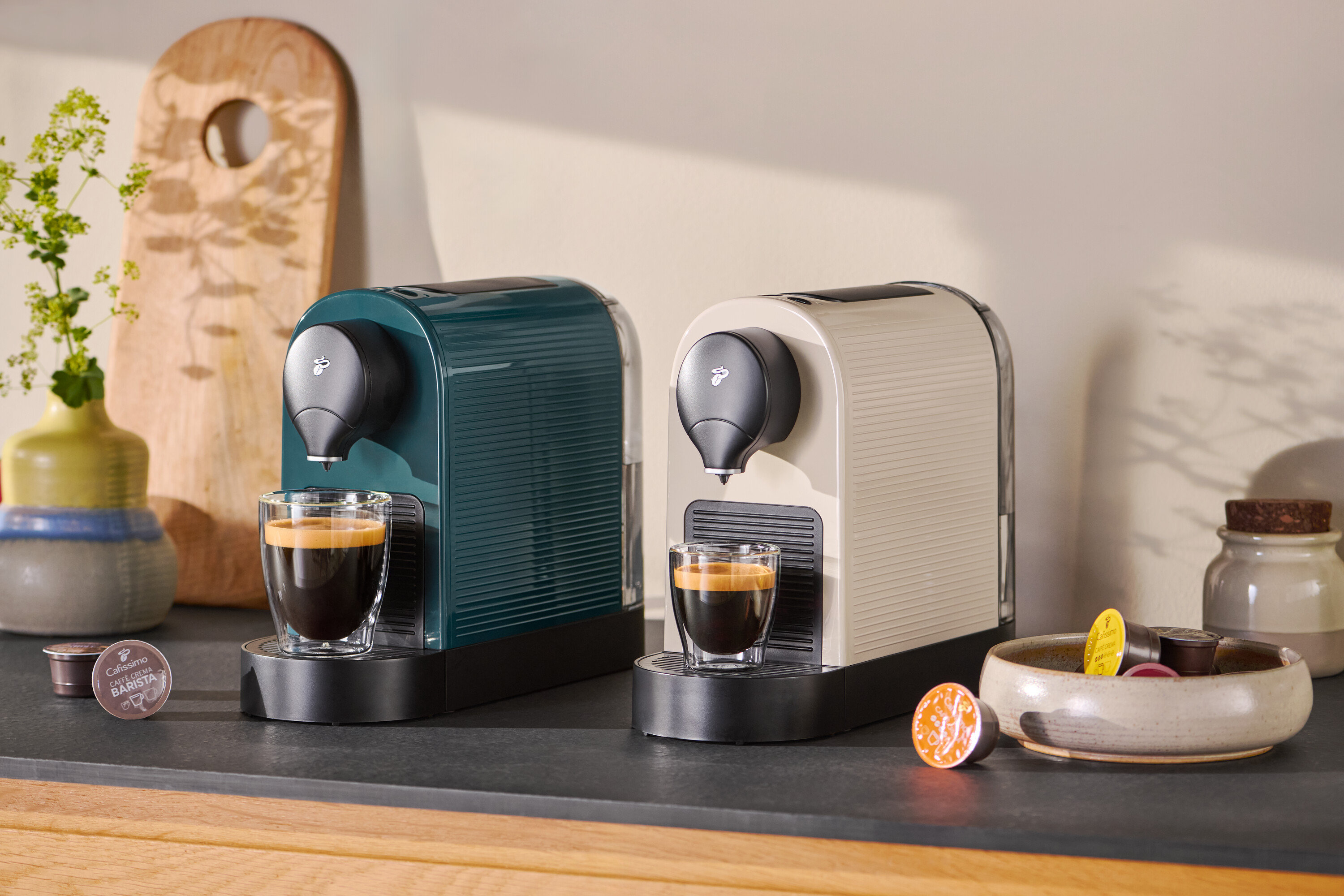 İki adet Cafissimo Pure kahve makinesi, biri petrol rengi ve diğeri bej, her ikisinde de birer fincan espresso var.