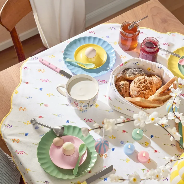 Yemek masası; tabaklar, yumurtalar, kupalar, çatal bıçak takımı, ekmek sepeti, reçel kavanozları, Paskalya süslemeleri ve çiçekli bir masa örtüsü dahil olmak üzere sofra takımı ile birlikte.