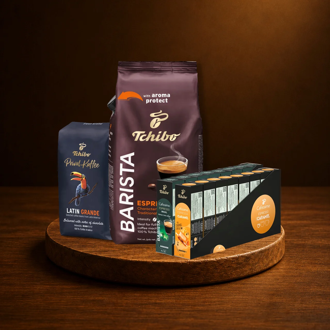 Ahşap tepside üç Tchibo kahve ürünü. Solda "Privat Kaffee Latin Grande" çekirdek kahve, arkada "Barista Espresso" çekirdek kahve, sağda "Cafissimo Espresso Caramel" kapsülleri.